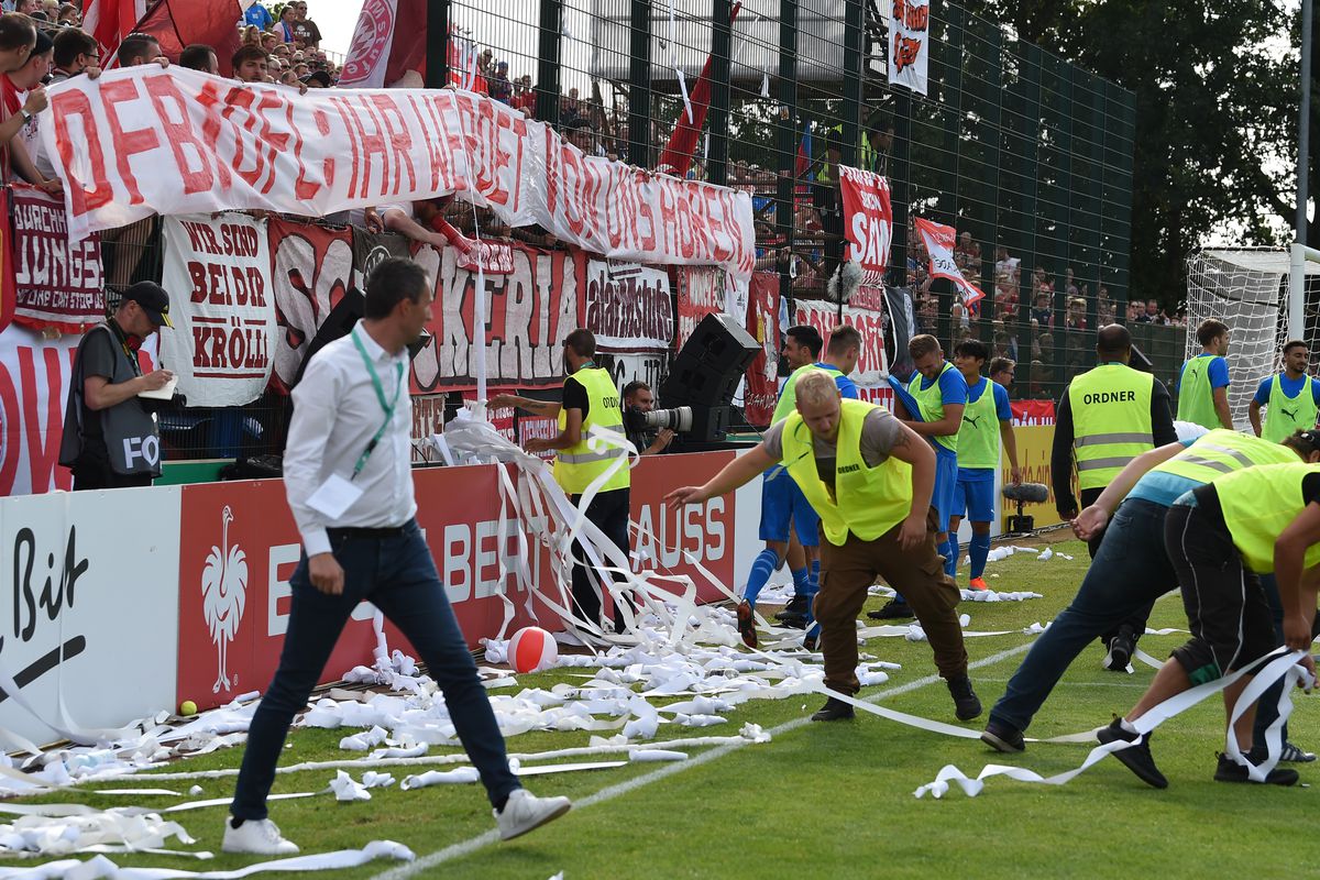 18 August 2018, Germany, Drochtersen: Soccer, DFB Cup, SV Drochtersen/Assel vs Bayern Munich, 1st round in Kehdinger Stadium. Folders clean the playing field after Bayern fans interrupted the game by throwing plastic balls and toilet paper rolls.