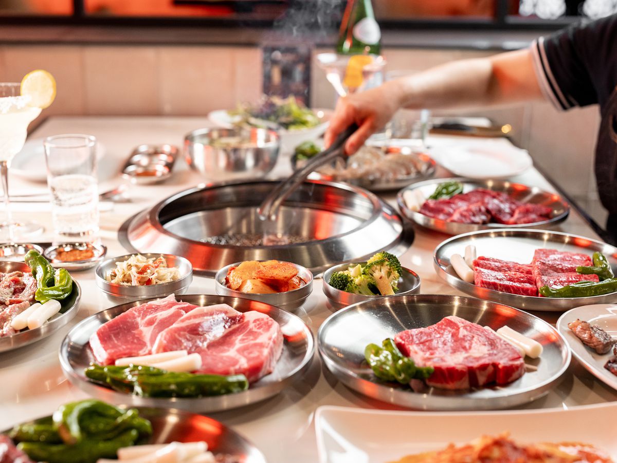 A table is set with various meats on white dishes at a Korean barbecue restaurant.