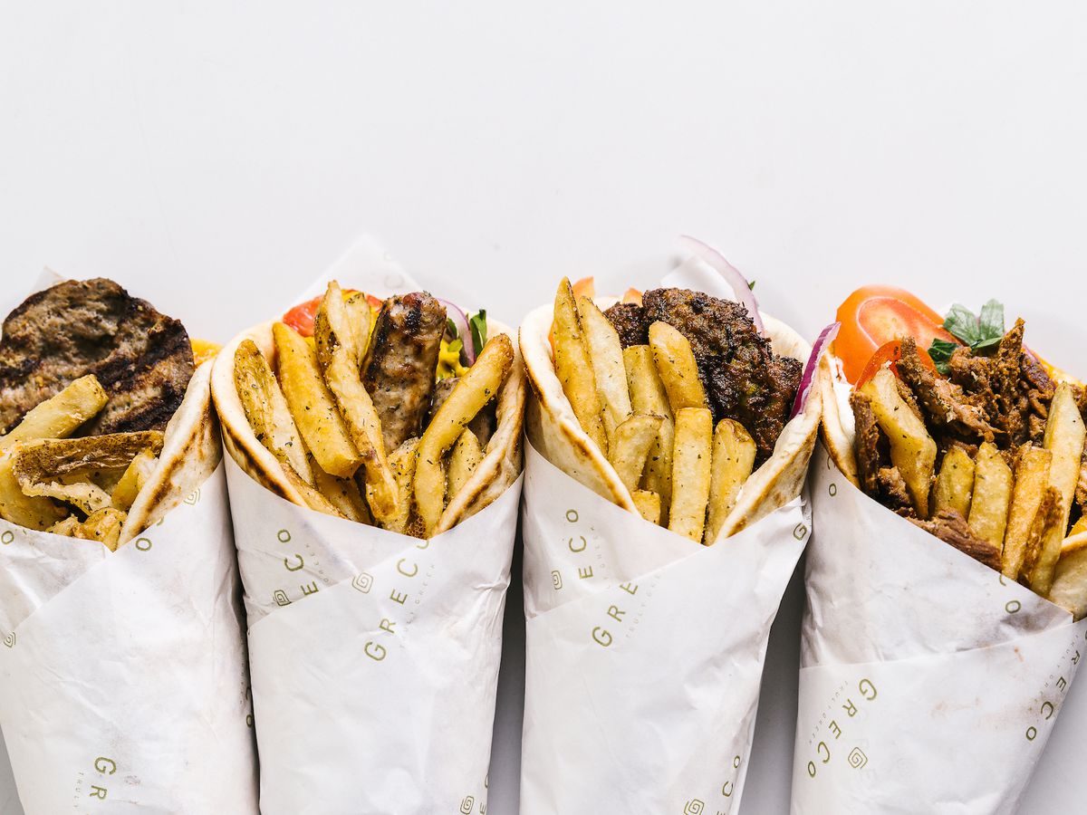 Four gyros lined up with meat, vegetables, and fries visible.