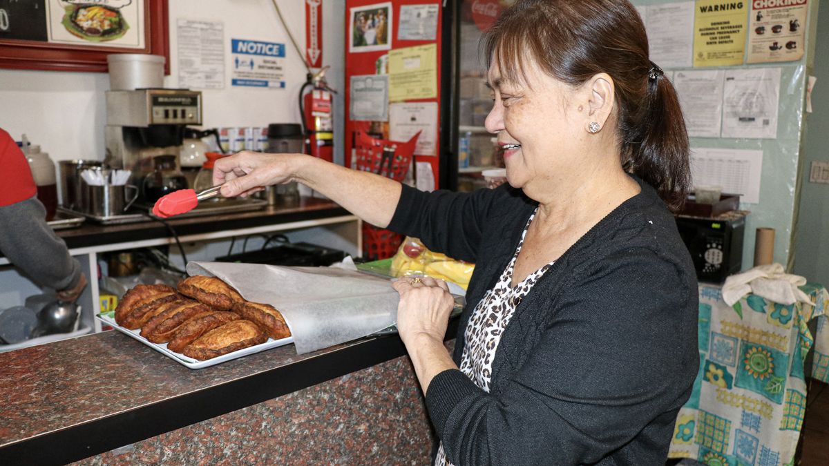 A restaurant owner grabs food with a pair of tongs.