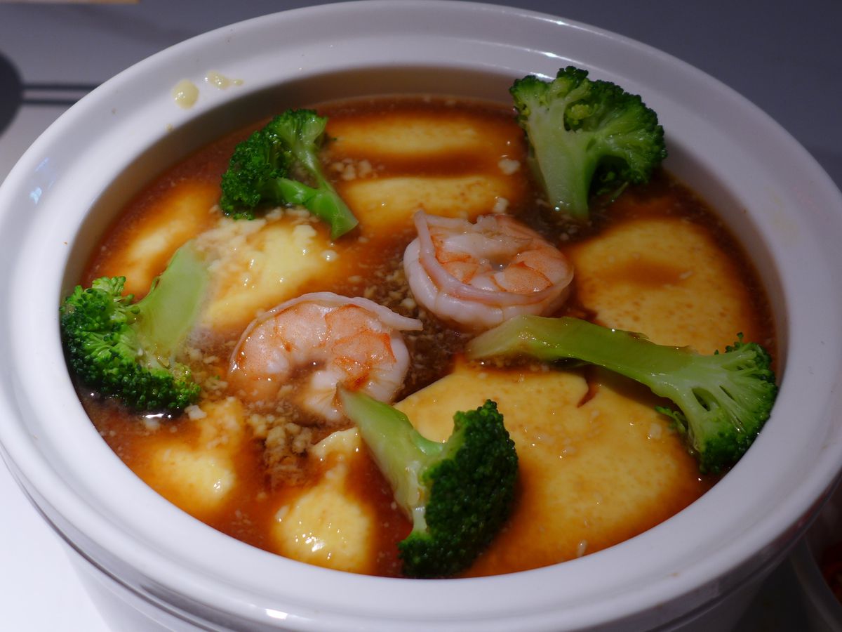 A white porcelain bowl filled with eggs, sauce, shrimp, and broccoli.