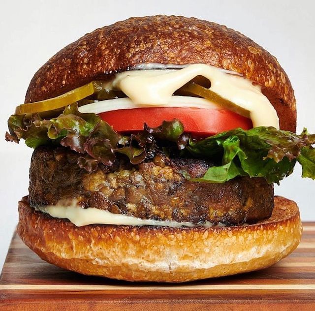 A photo of the Fermenter burger with a millet and black lentil tempeh patty on a wooden cutting board against a white background.