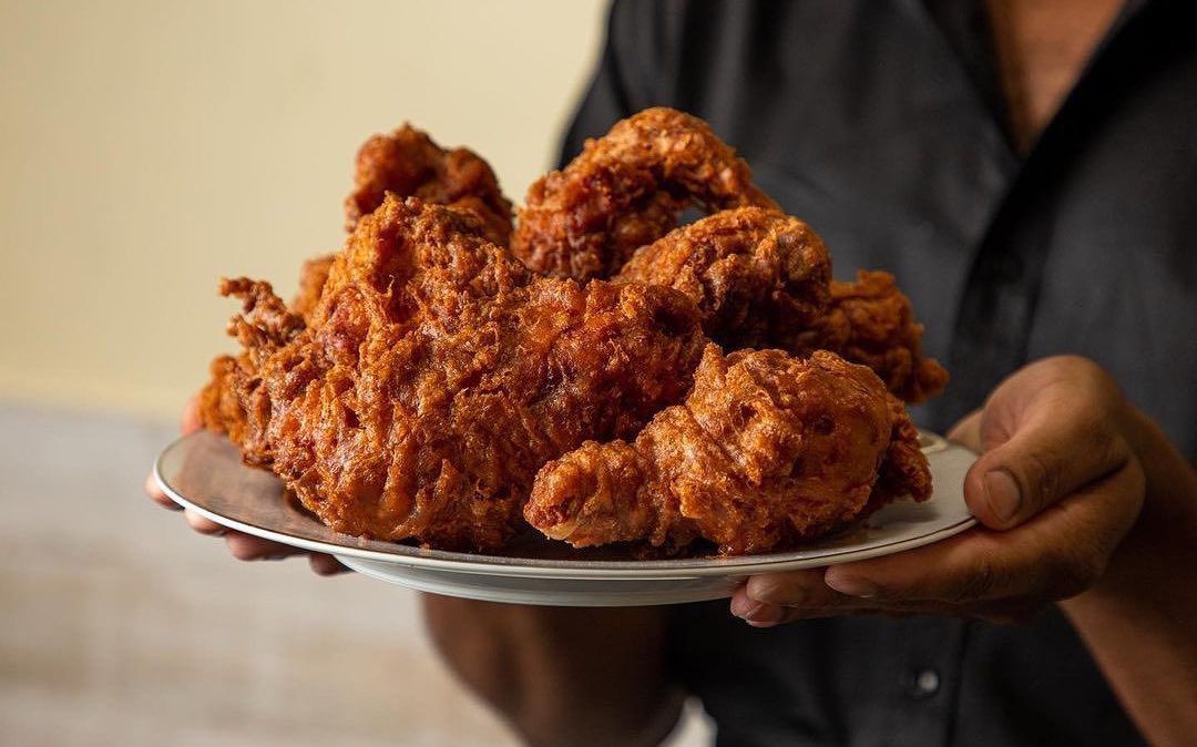 A pair of Black hands holds a white plate filled with fried chicken.