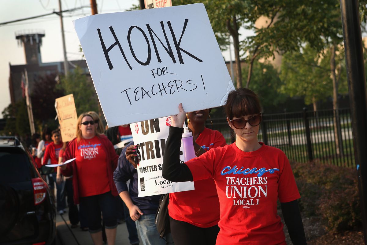 A dark-haired woman wearing sunglasses and a red Chicago Teachers Union shirt holds a sign that reads “Honk for teachers.”