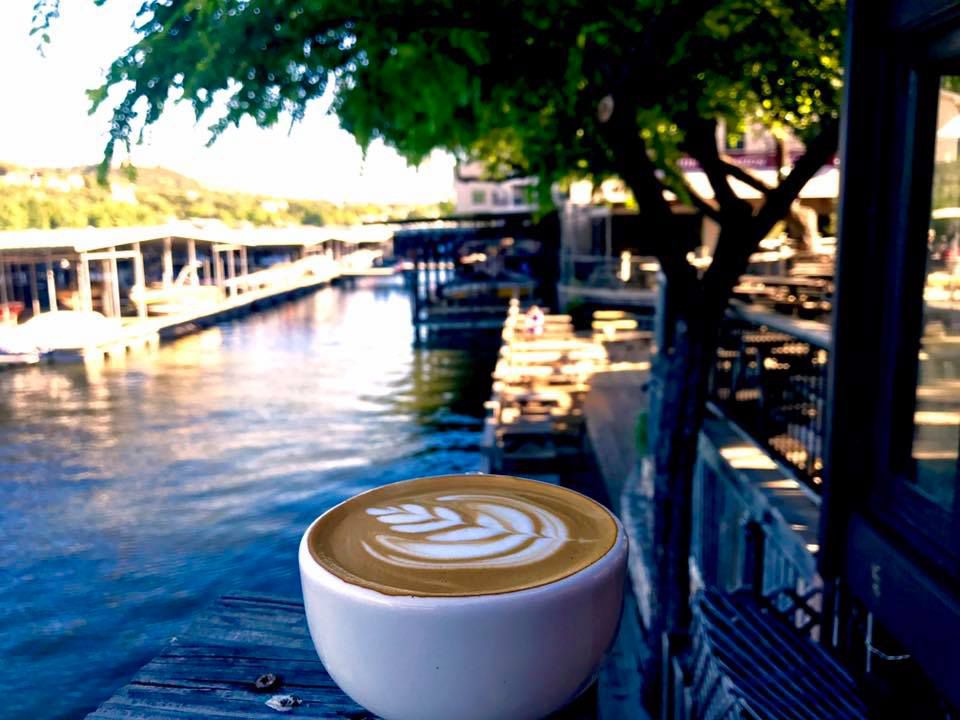 A cup of coffee on a ledge overlooking water.