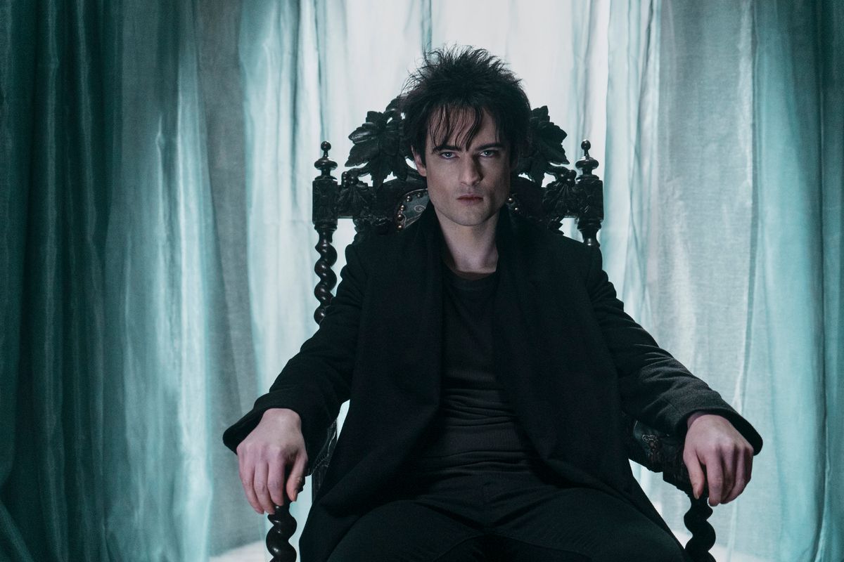 Tom Sturridge as Dream sits in an ornate chair in front of a curtain in a photo from Netflix’s The Sandman