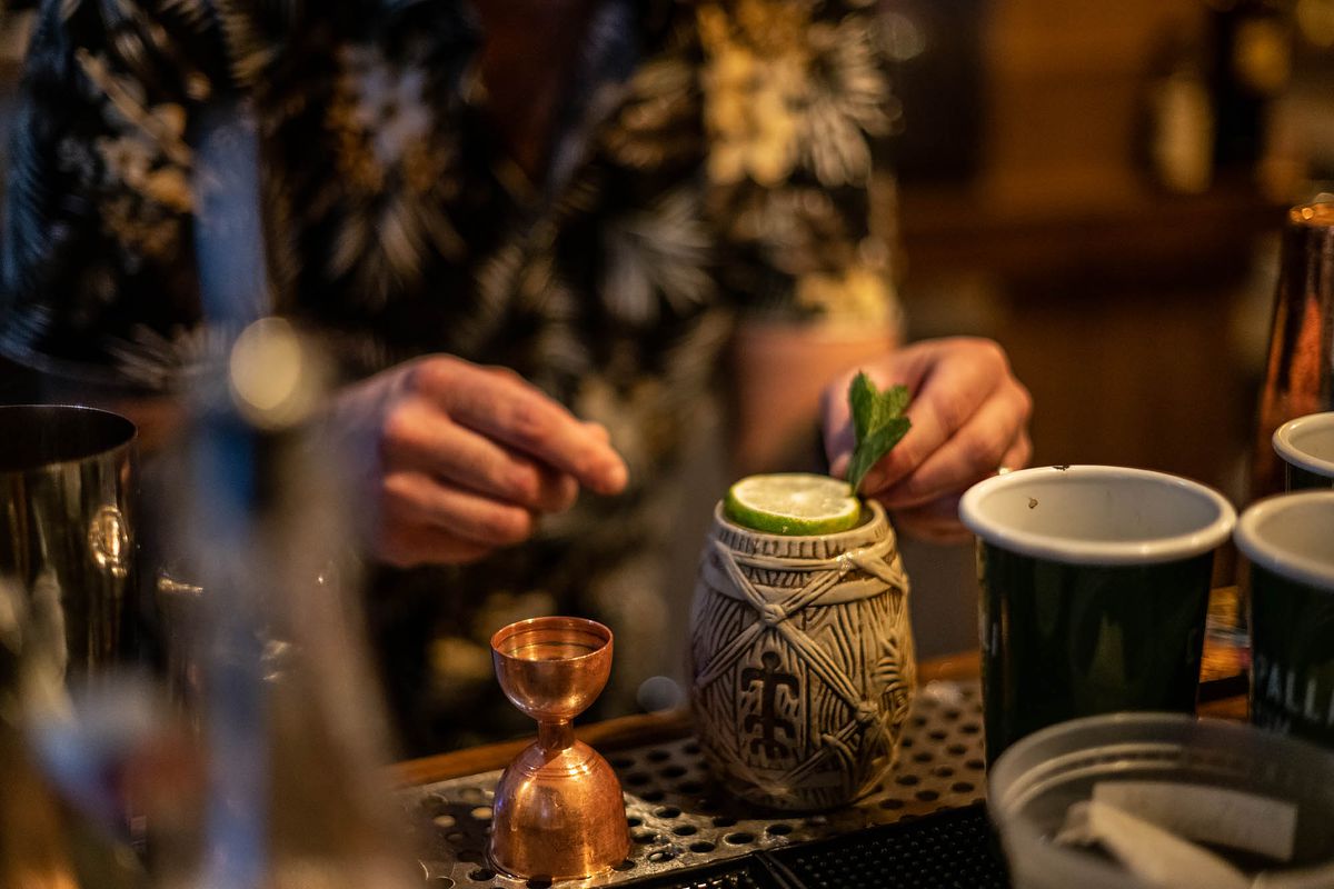 An unseen bartender prepares a cocktail drink in a barrel-shaped vessel.