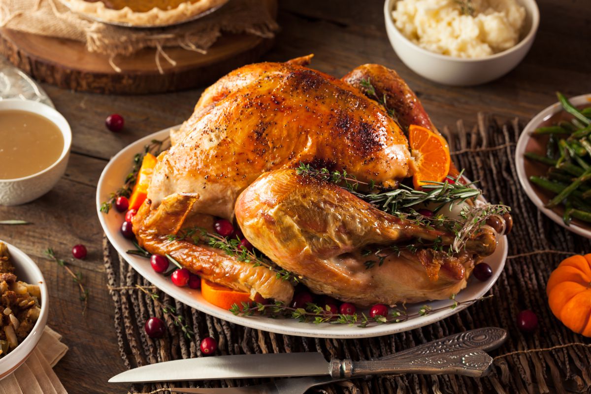 A roasted turkey sits on a plate garnished with sprigs of rosemary, cranberries, and other herbs on a wooden table.