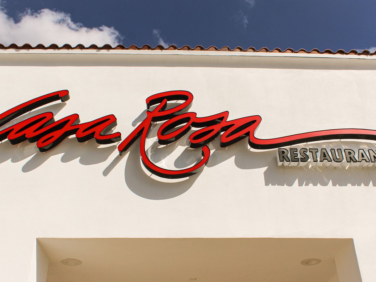 The exterior of Casa Rosa Tex Mex, an off-white plaster exterior with a sign displaying the restaurant’s name in red cursive letters. 