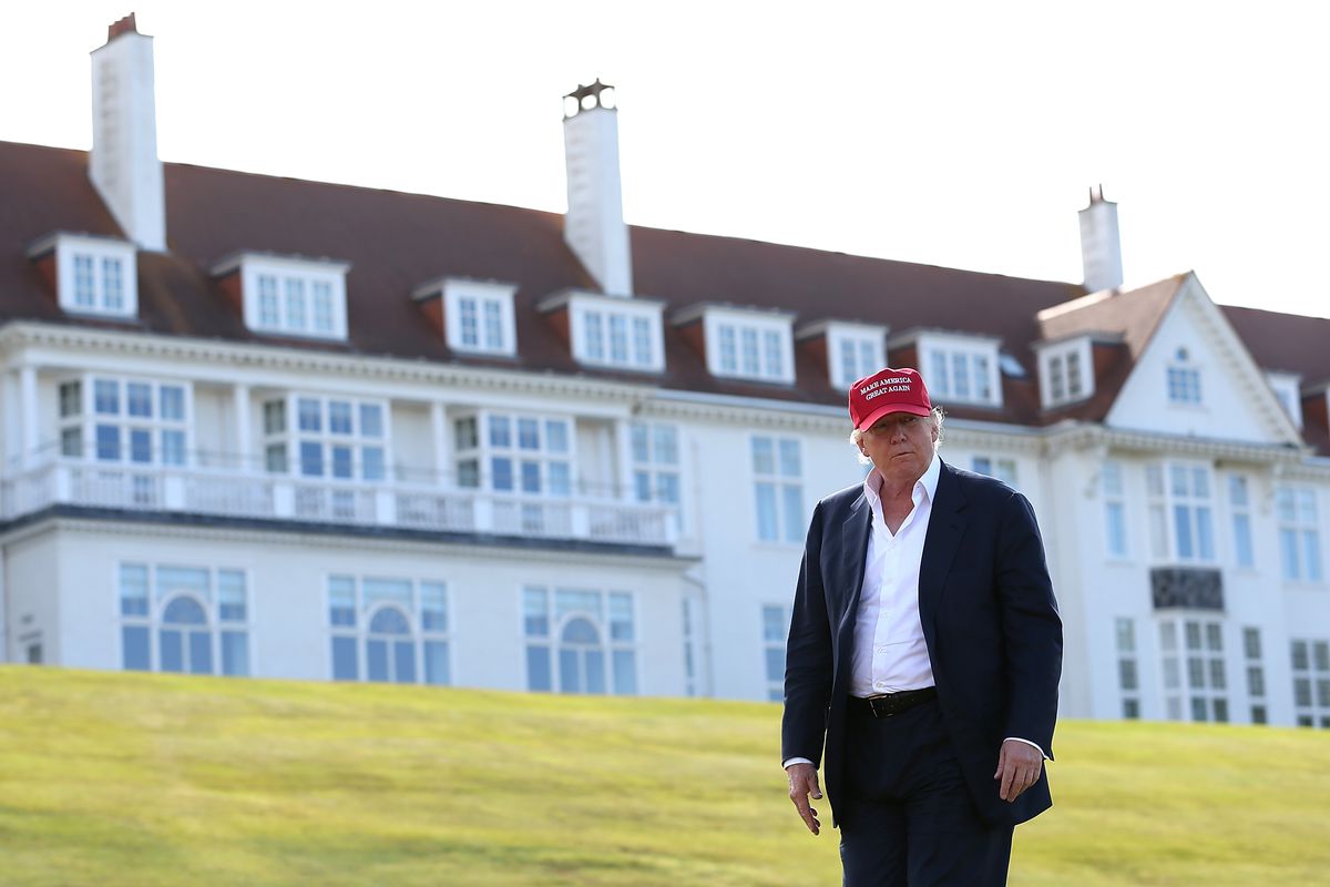 Donald Trump stands on the lawn of his Ayr resort in a dark suit and a red “Make America Great Again” baseball cap.