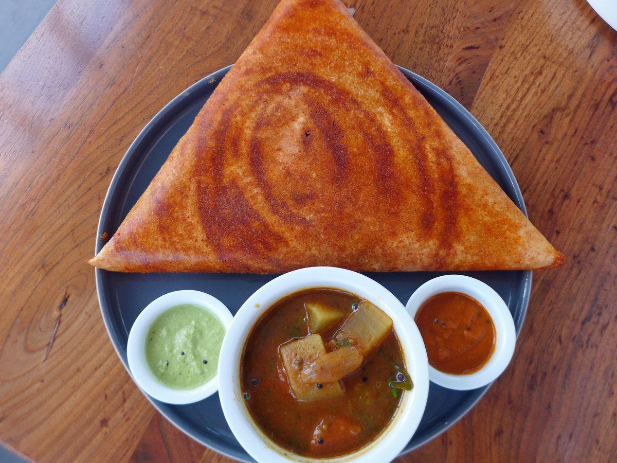 A perfect equilateral triangle of a dosa, with three sauces underneath in tiny bowls.