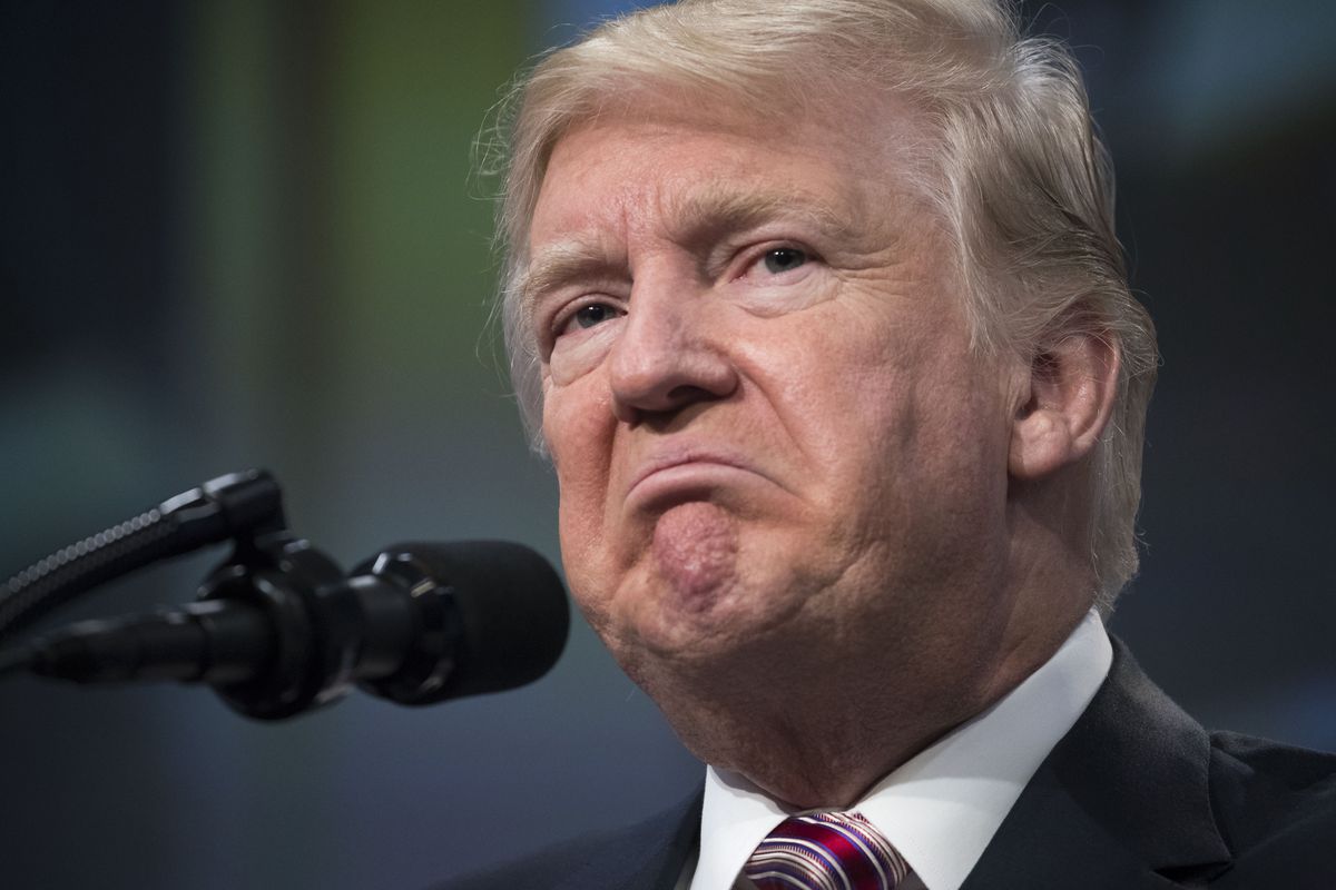 President Donald Trump stands in front of a microphone making a frowning face.
