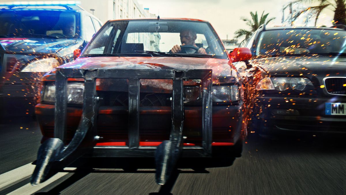 A red automobile with a metal cowcatcher is sandwiched between two cop cars in Lost Bullet.