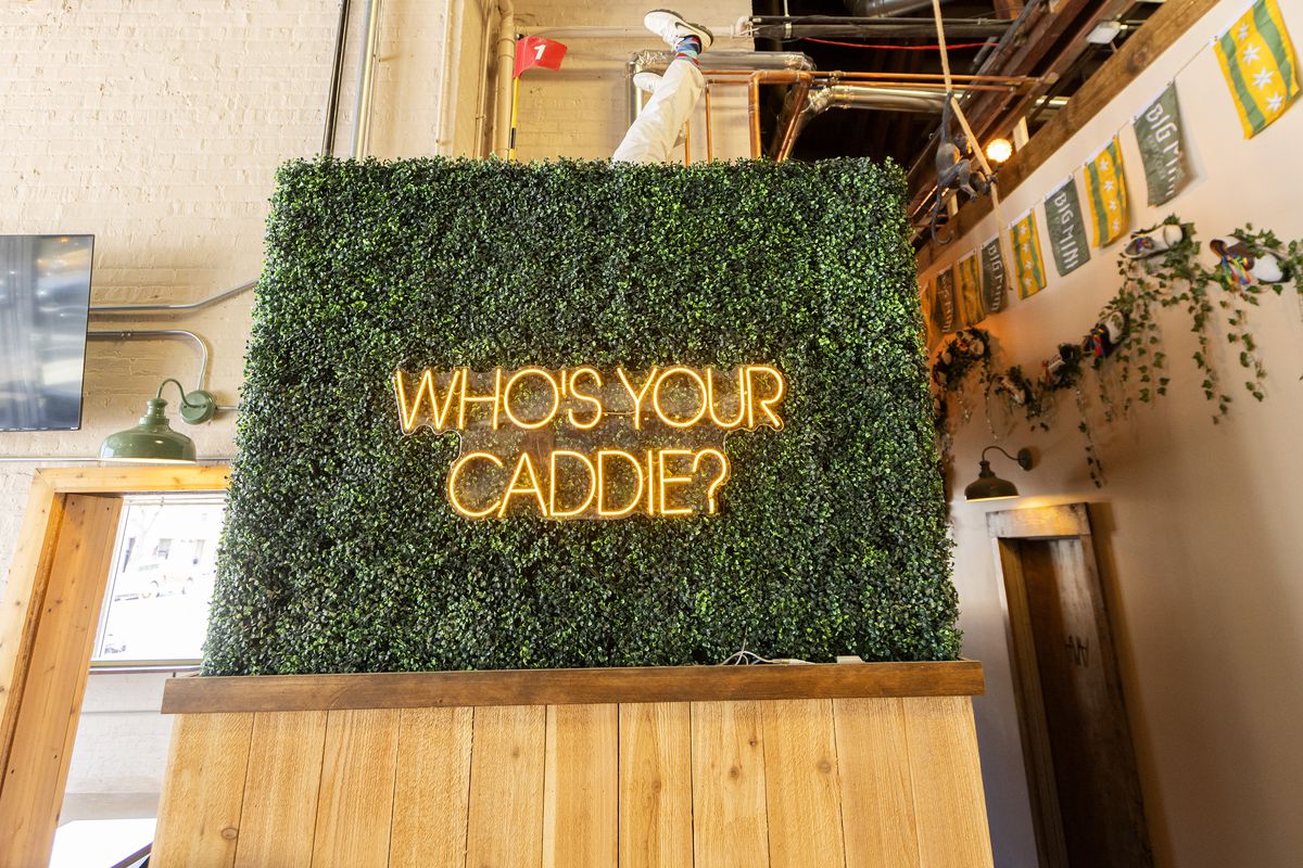 A yellow neon sign reads “Who’s your caddie?”
