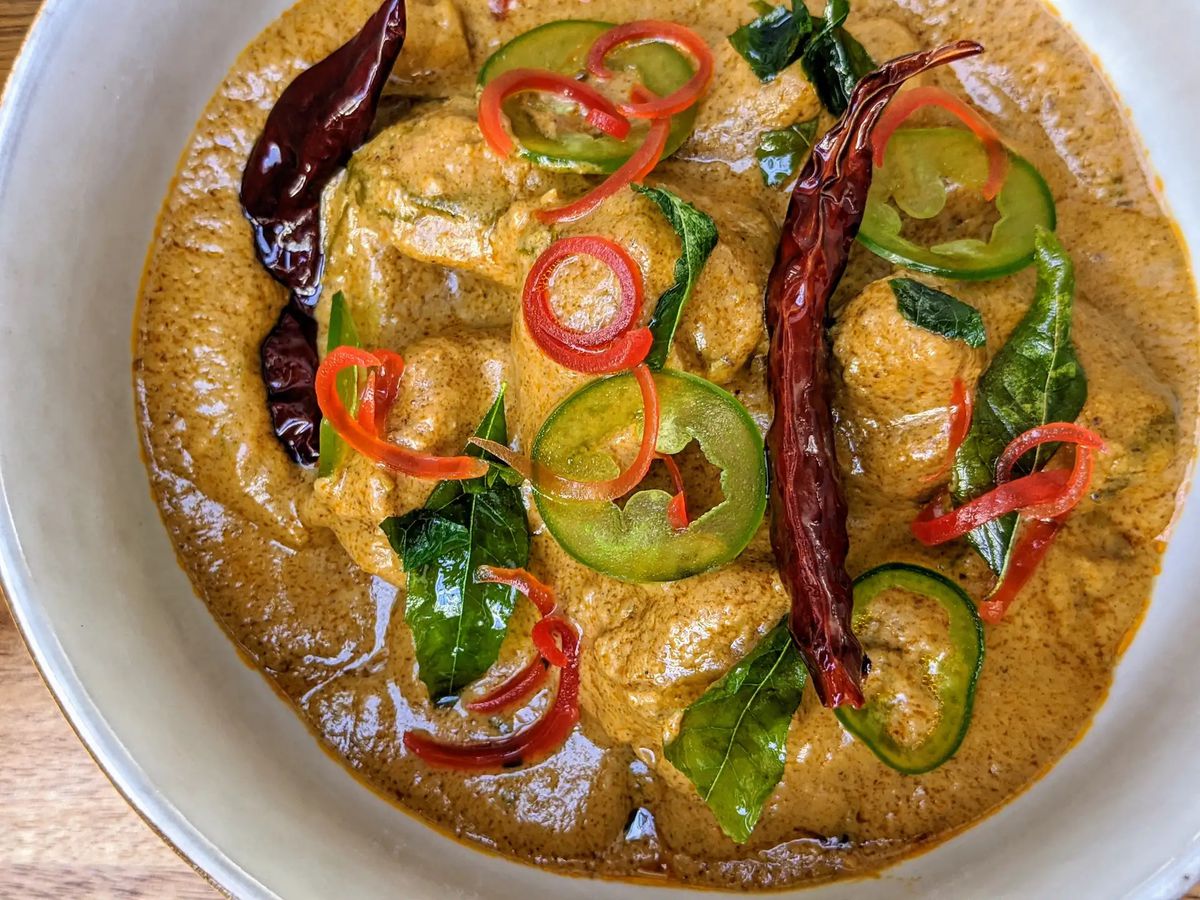 A white bowl full of curry with chiles and chicken.