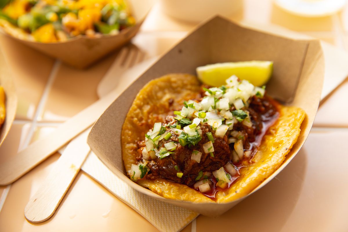 A to-go boat contains a juicy beef taco topped with cilantro and onion