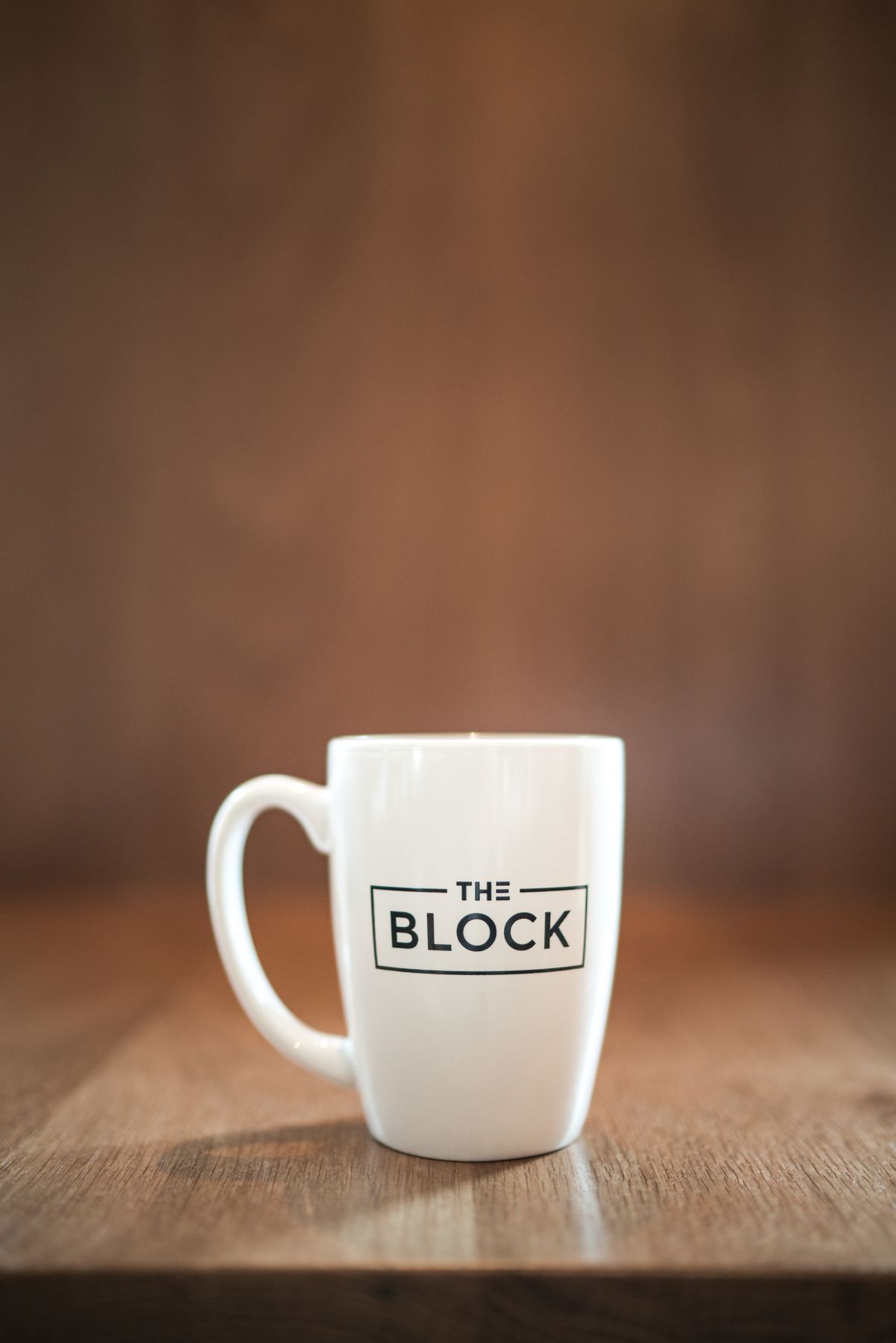 A white mug on a wooden countertop, with the logo of the restaurant “The Block” on it.