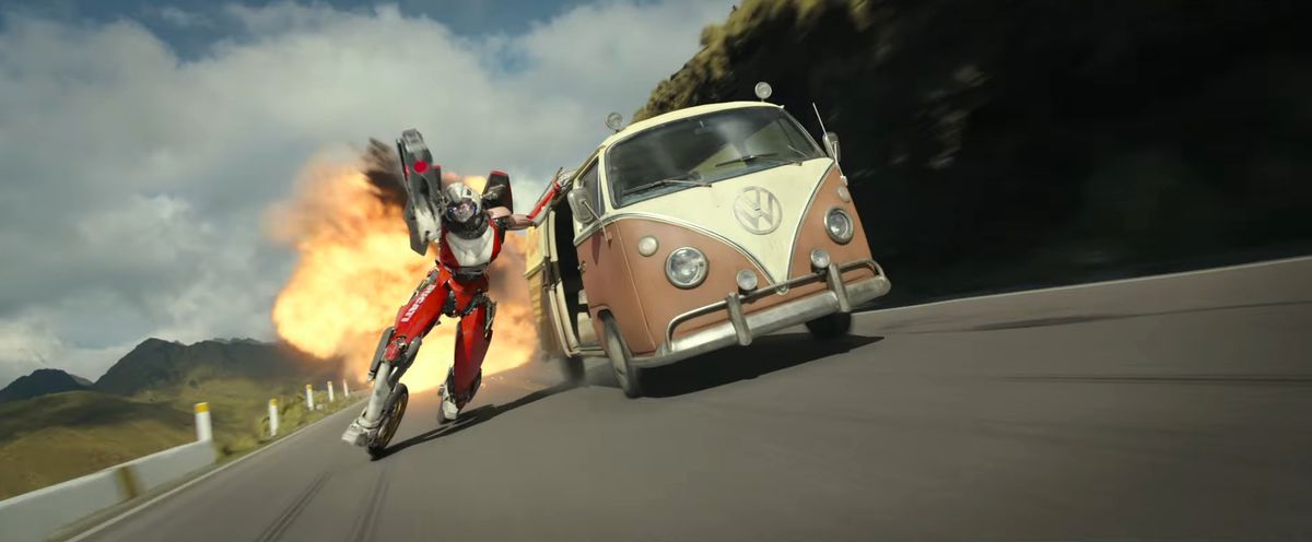 Acree the transformer uses her motorcycle feet to ride a brown VW bug away from an explosion during a car chase in Transformers: Rise of the Beasts