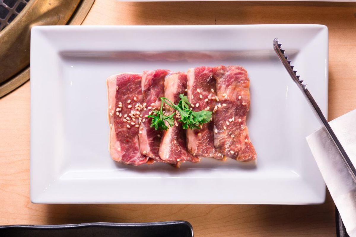 A plate of raw meat garnished with parsley and ready to be grilled at Gyu-Kaku