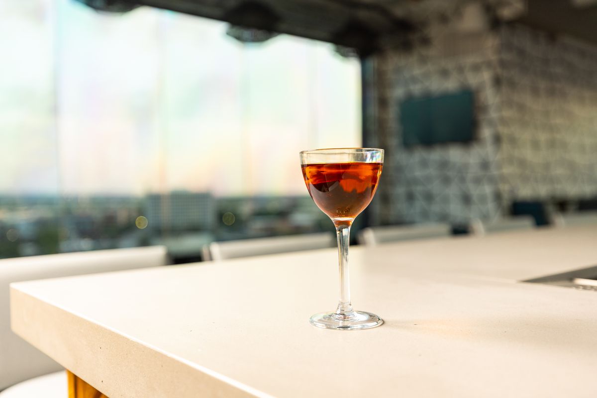 A coupe with a Manhattan in it sits on an off-white bar top with the skyline of Dallas in the relief.