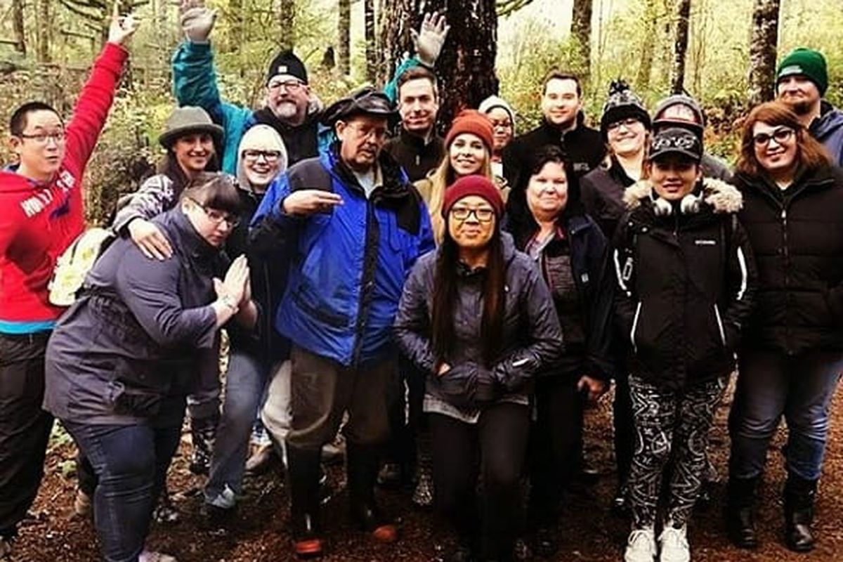 Around 15 people stand in the woods posing for a photograph.