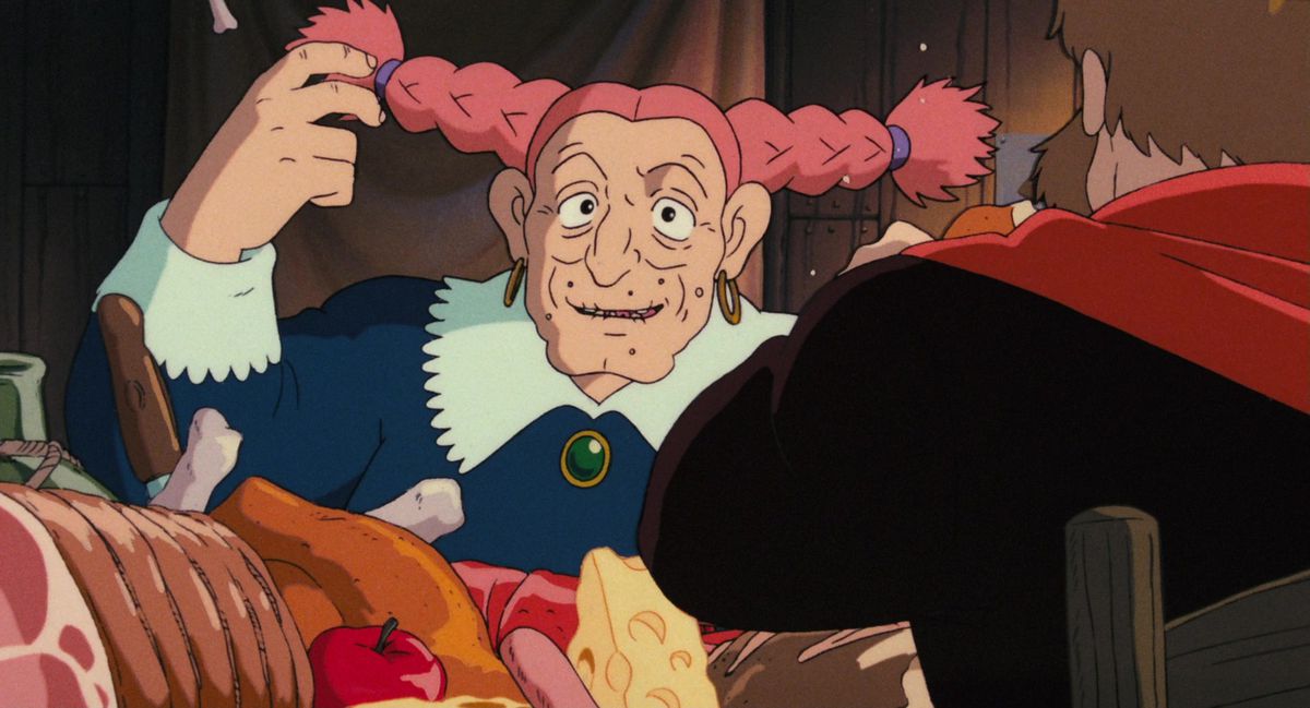 The pirate queen Dola, an older woman with twin pink horizontal brains, sits at a table full of food in Hayao Miyazaki’s Castle in the Sky.
