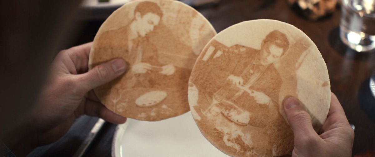 Two pieces of flatbread with images of Nicholas Hoult taking iphone pics of his food in The Menu