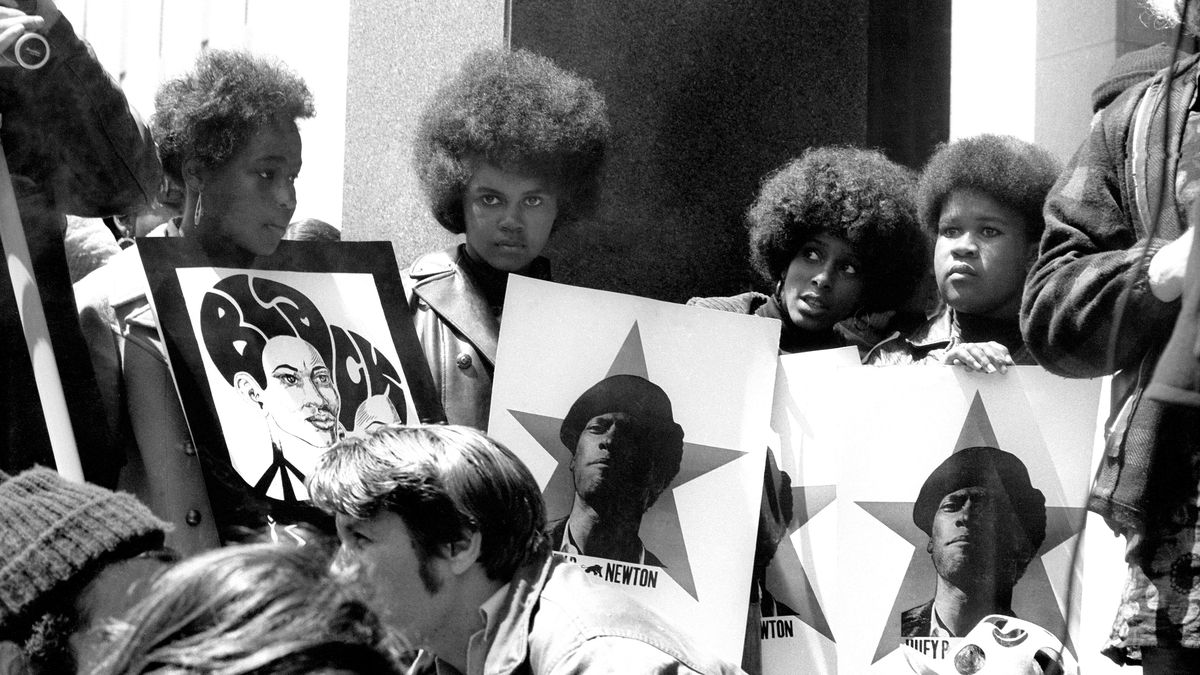 A group of Black women hold signs showing a picture of Black Panthers Party co-founder Huey P. Newton at a protest in 1969.