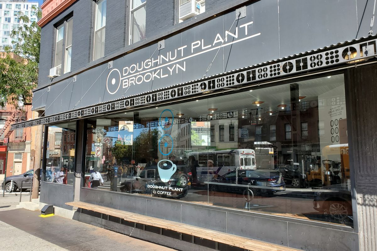 The exterior of a shop with a black sign in front that reads doughnut plant
