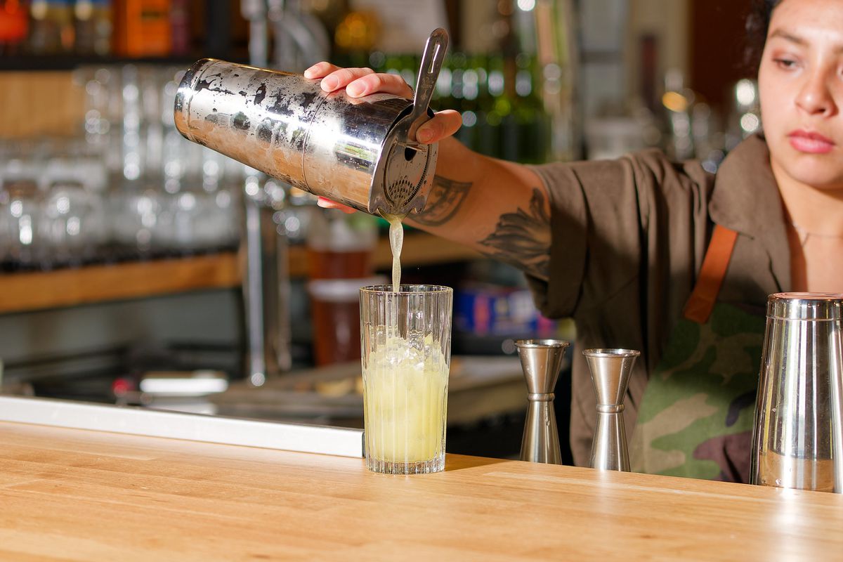 A bartender pouring a cocktail from a mixer into a glass.