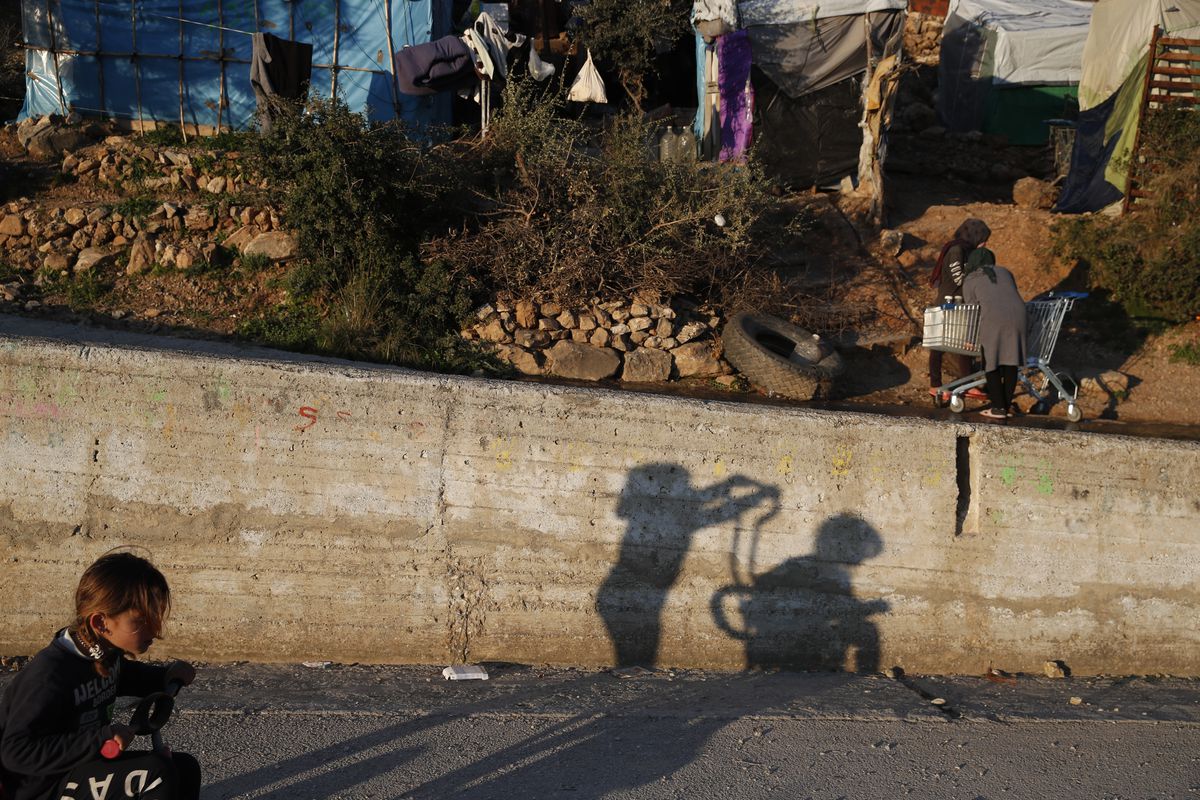 Children play as others put water on a shopping cart outside the perimeter of the overcrowded refugee camp at the port of Vathy on the eastern Aegean island of Samos, Greece.