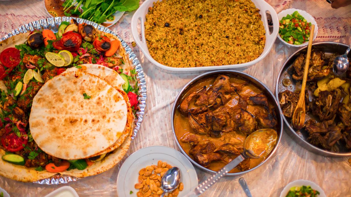 A table set with an iftar meal: roasted veggies and meats with roti, cooked yellow rice, stewed meats, and peanuts. 
