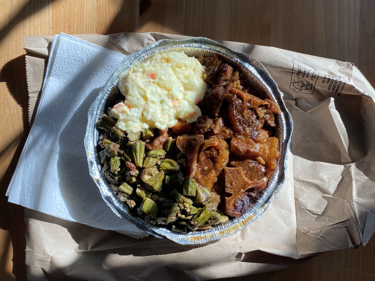 An overhead photograph of a takeout tray brimming with oxtail, okra, and potato salad.