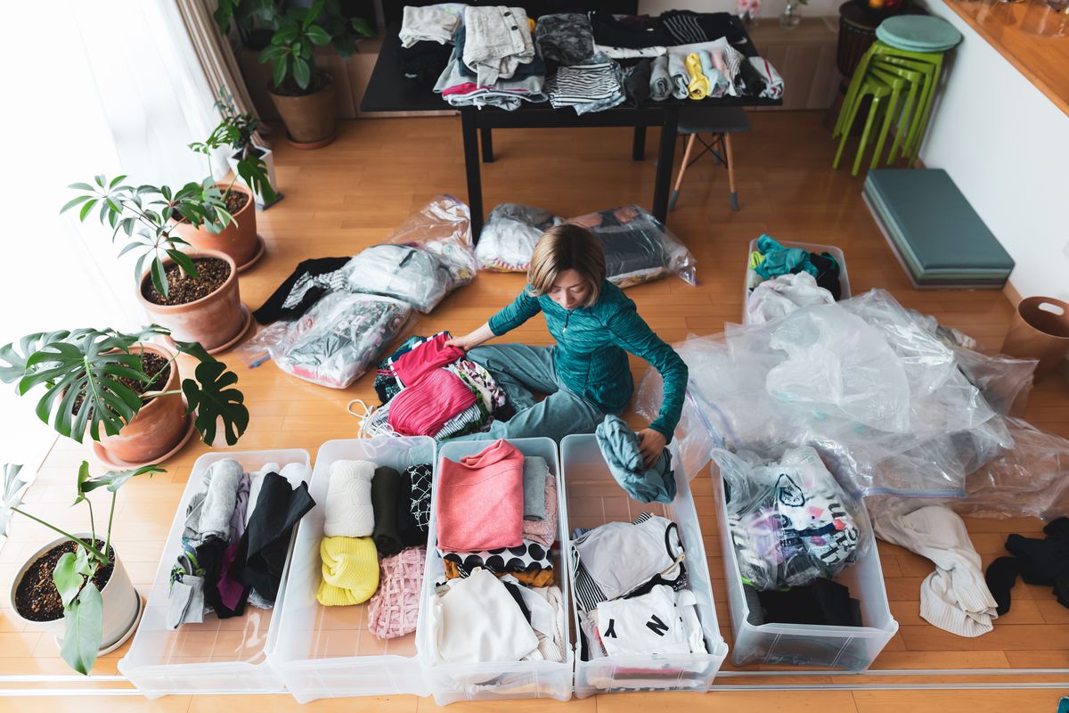A person sitting on the floor of their house surrounded by organized clutter.