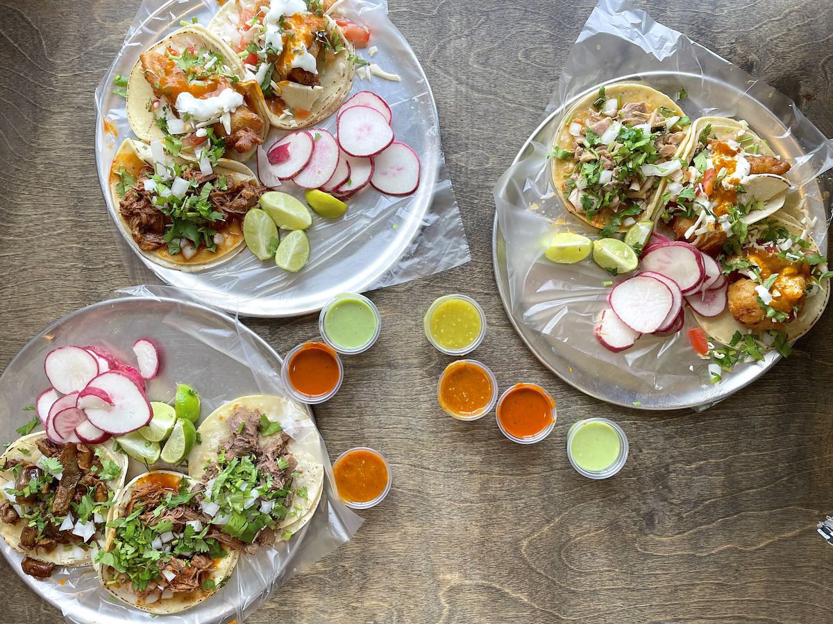 An array of tacos with radishes, lime, and salsas