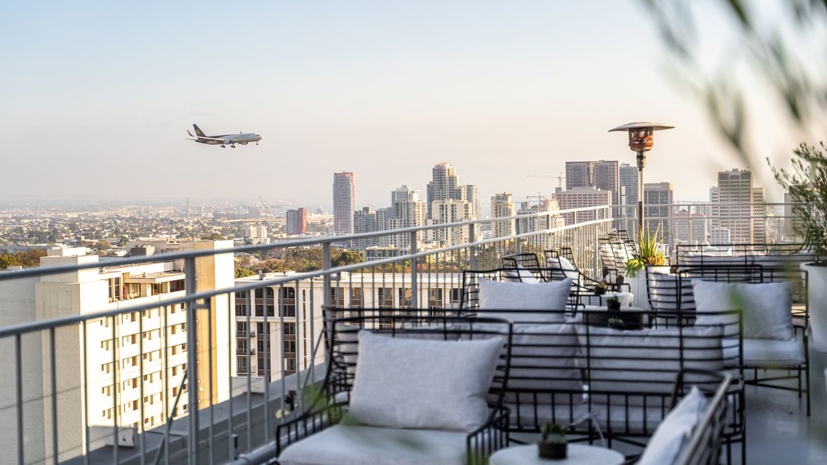 An airplane flies above a rooftop patio.