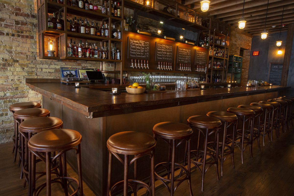 A rectangular dark wooden bar surrounded by brown backless bar stools.