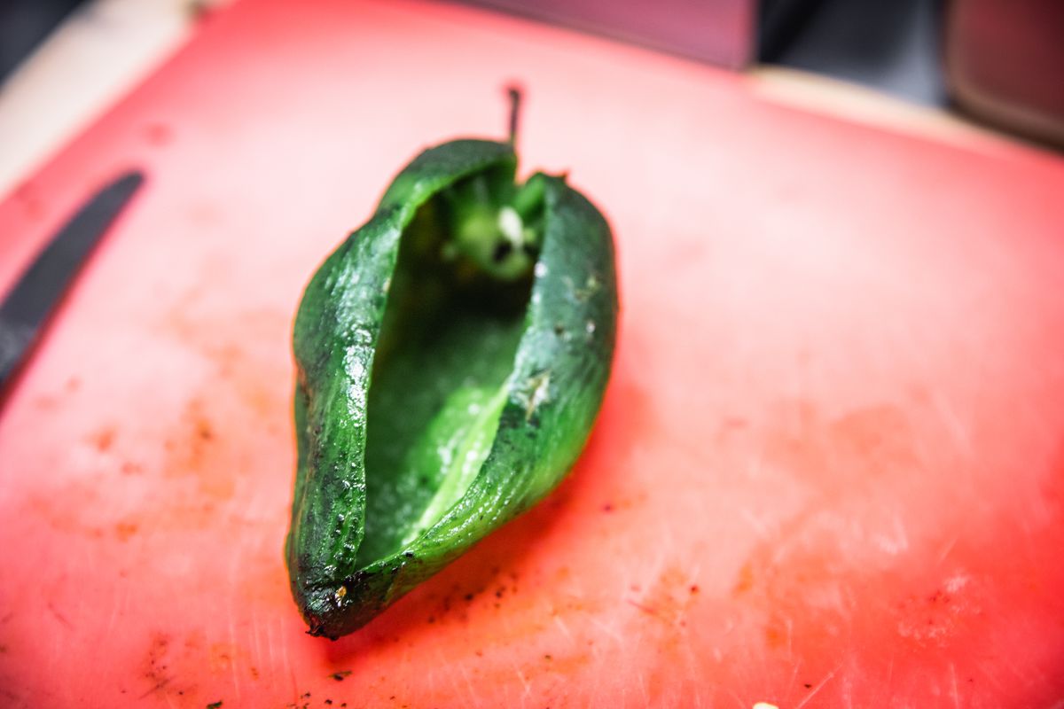 A green chile roasted and split open on a red cutting board.