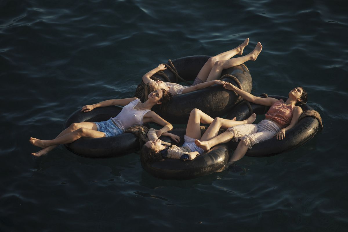 The women of Mayday lounge on floating inner tubes on the ocean, holding hands to stay together