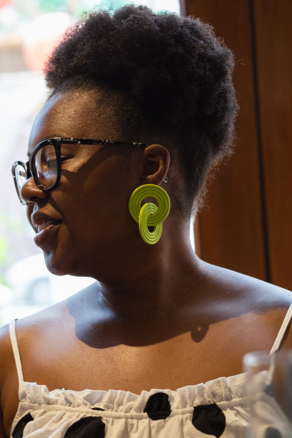 A woman in profile wearing glasses shows off her green earrings.