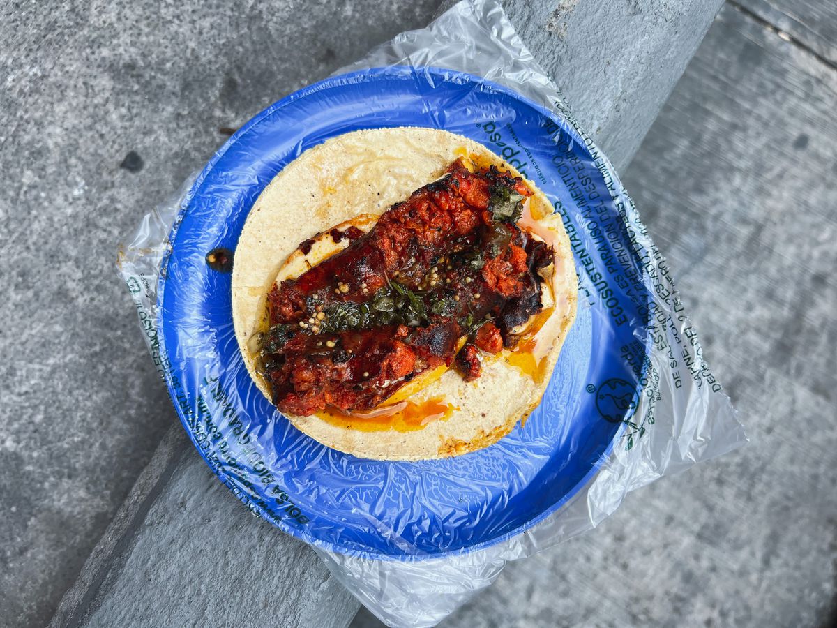 A taco on a plastic-wrapped plate, topped with deep red stewy meat.
