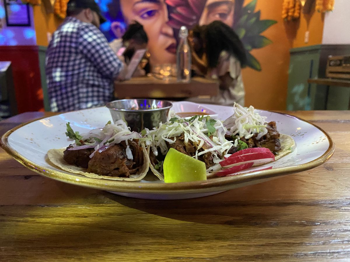 Three beef birria tacos sit on a plate next to a cup of consomme and salsa de arbol