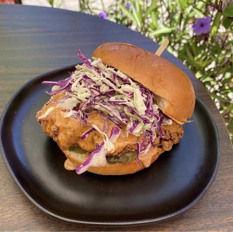 An open-faced fried chicken sandwich with lots of slaw and sauce.