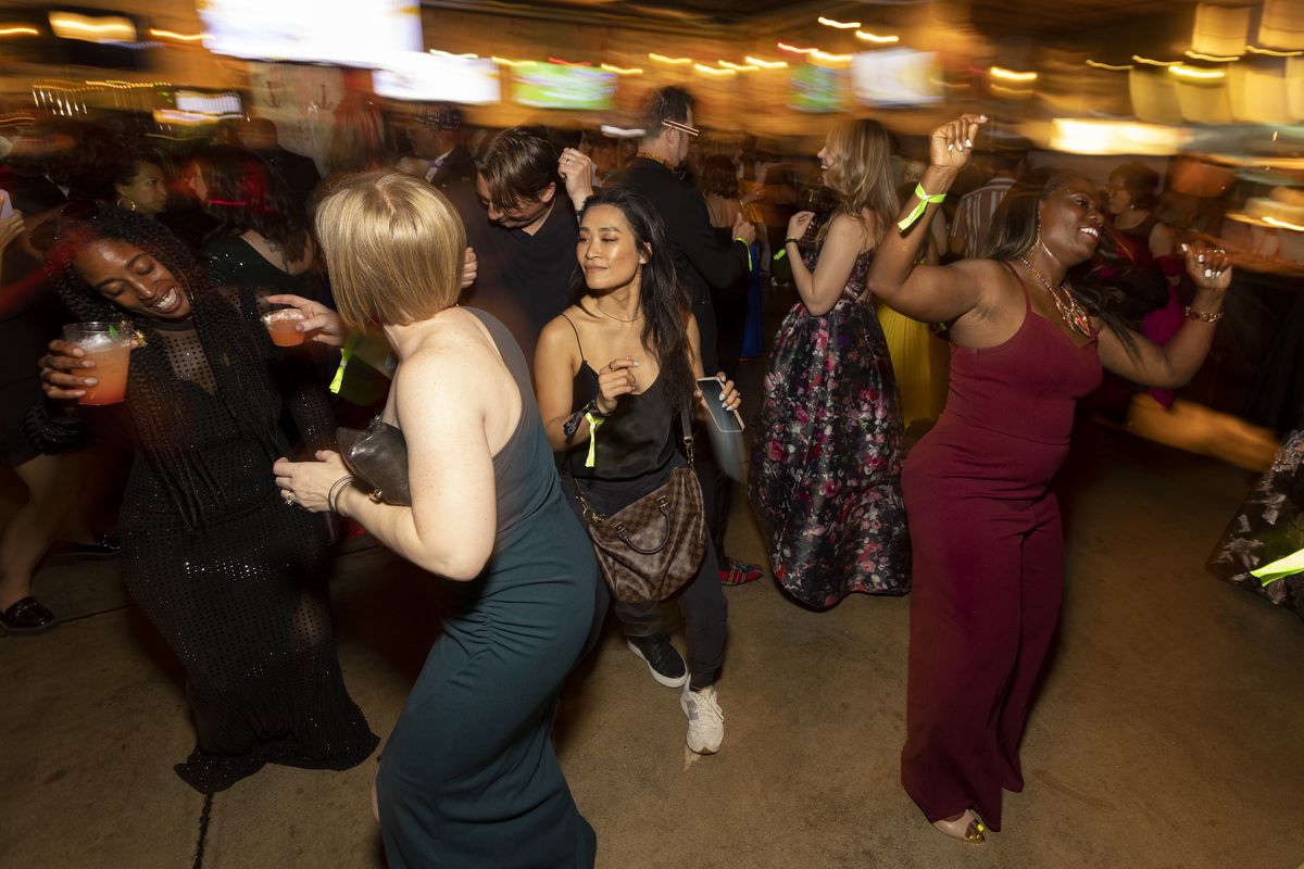 A group of women in formal dresses dance inside a cleared-out restaurant space.