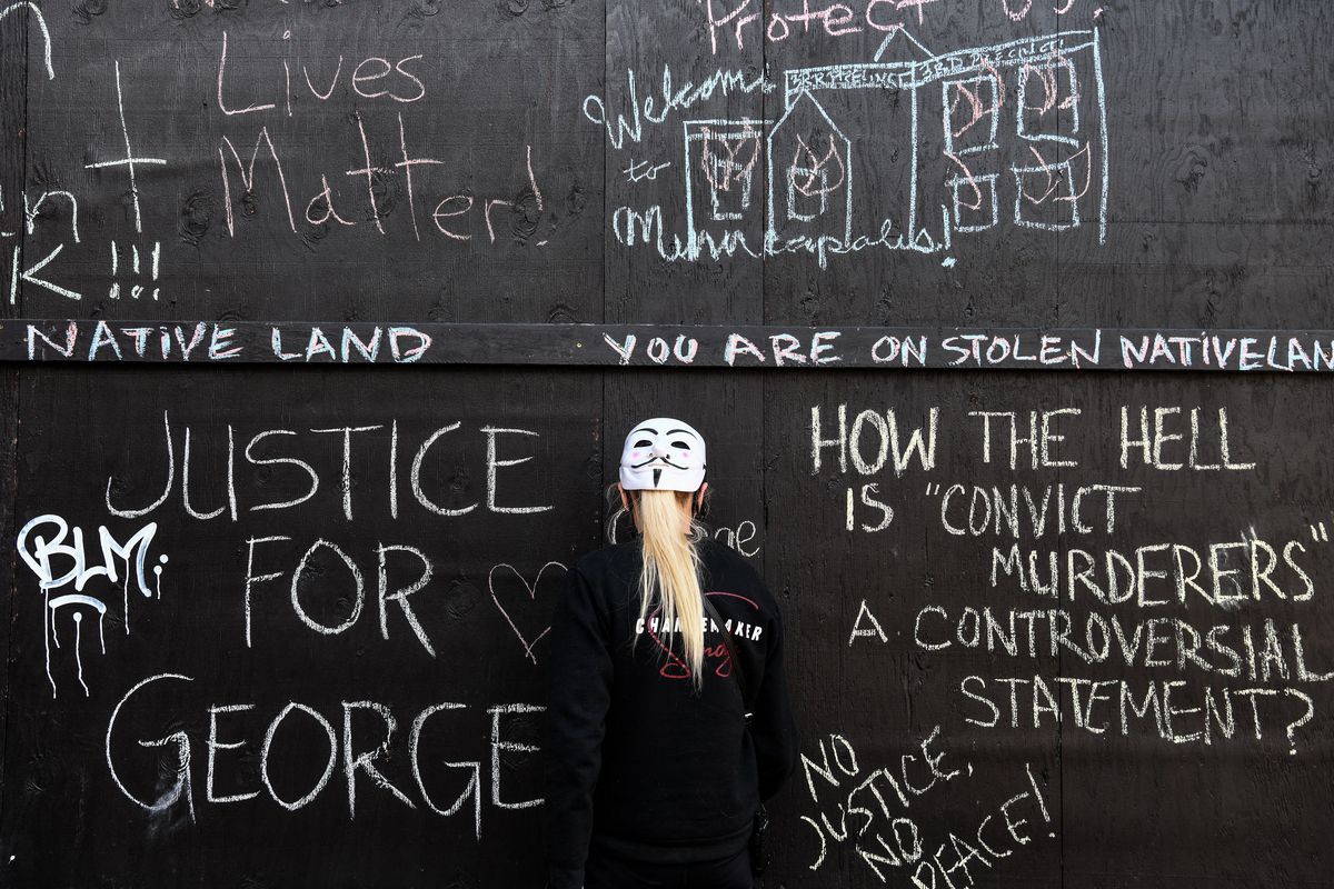 A demonstrator stands in front of a wall with chalk messages demanding justice for George Floyd. 