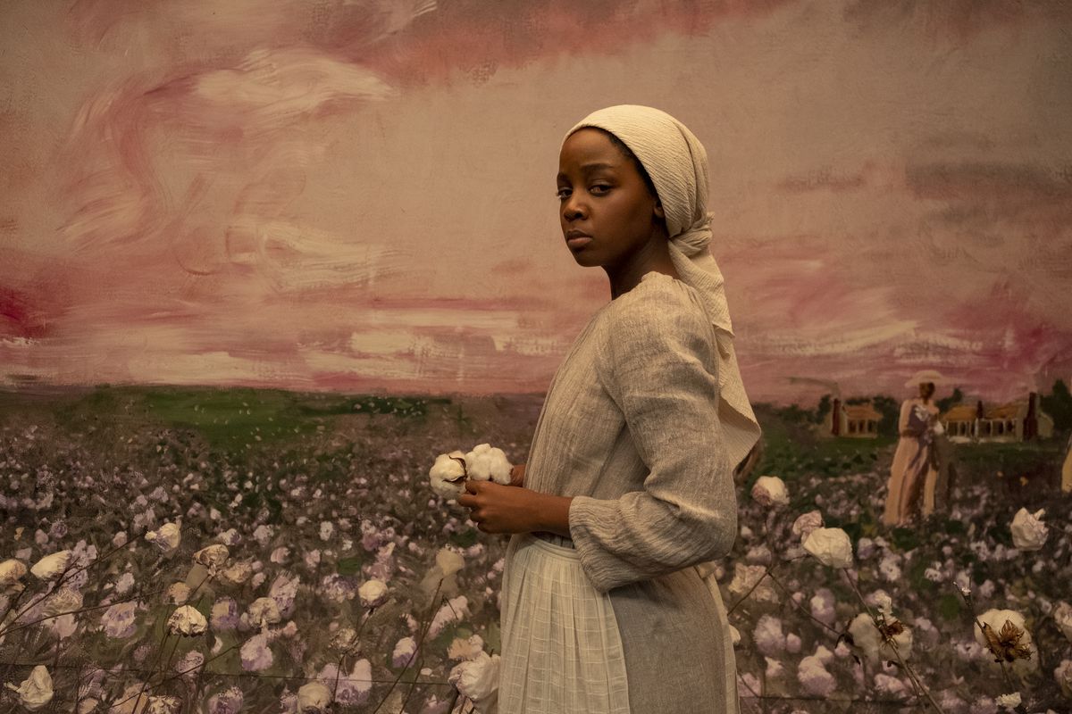 Cora, played by Thuso Mbedu, looks directly at the viewer in front of a mural of a cotton field.