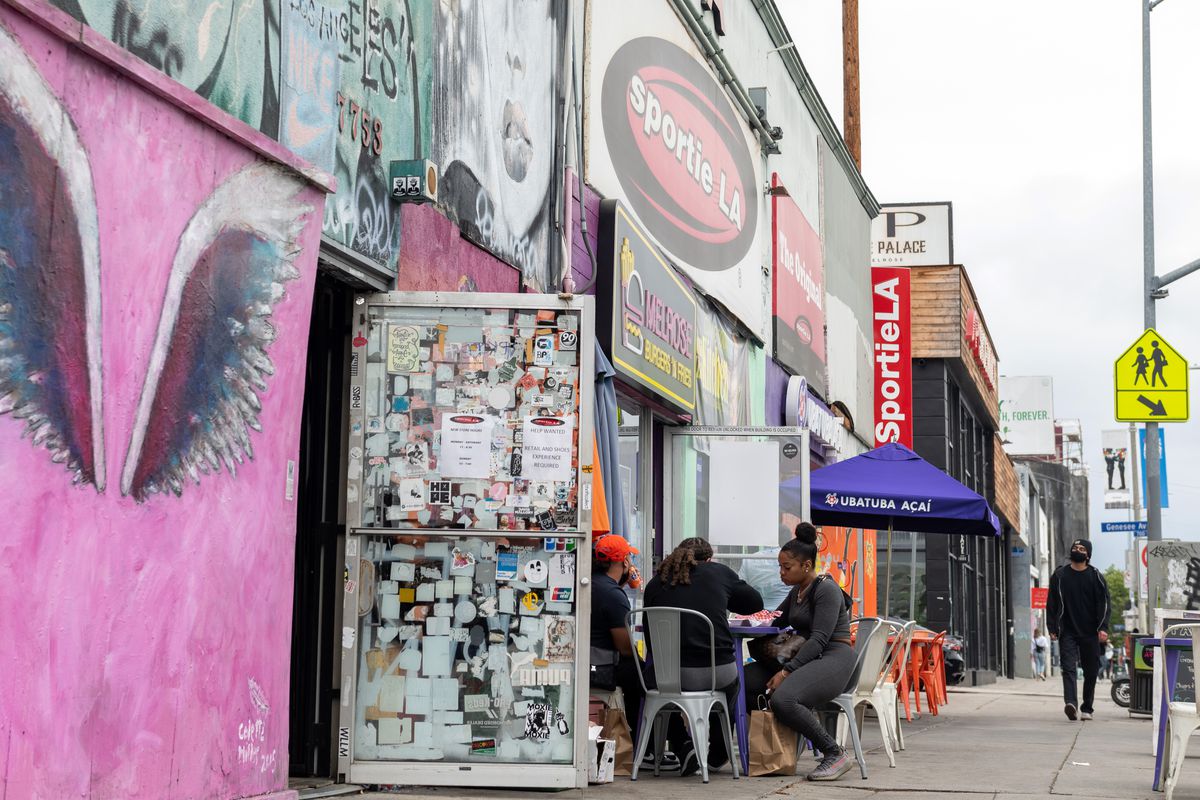 Diners sit outside on Melrose Avenue in LA with colorful building.