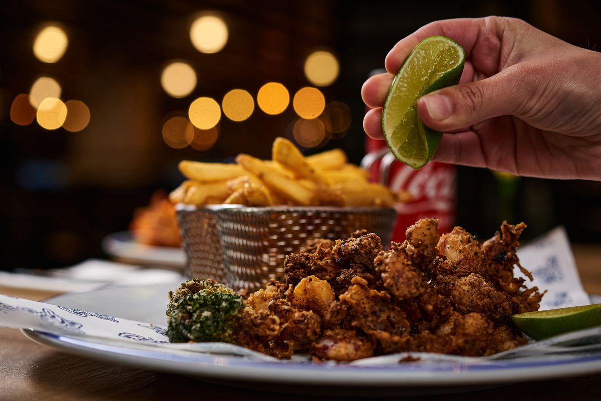 A hand squeezes lime on a plate of fried calamari and fries.