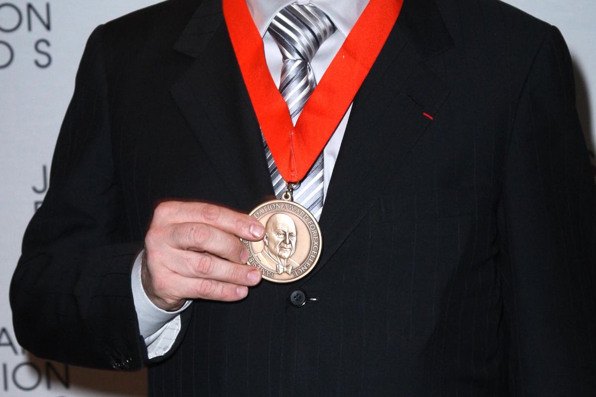 Photo shows someone holding up James Beard award medal, on ribbon around their neck.