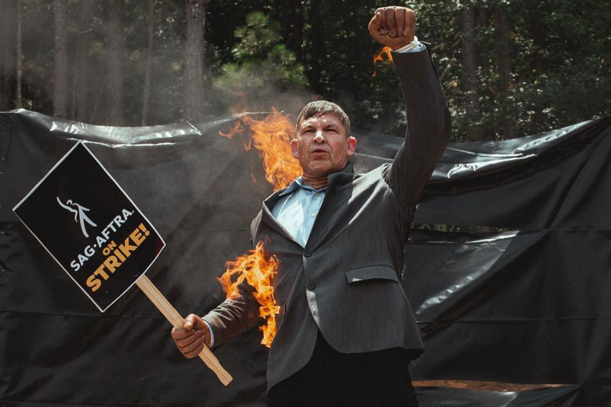 Stunt actor Mike Massa, wearing a suit and holding a strike sign, sets himself on fire at Atlanta picket line.